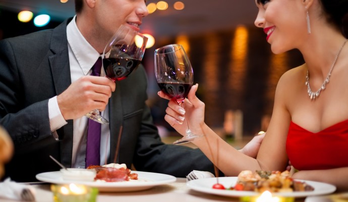 hands of couple toasting their wine glasses over a restaurant table during a romantic dinner.